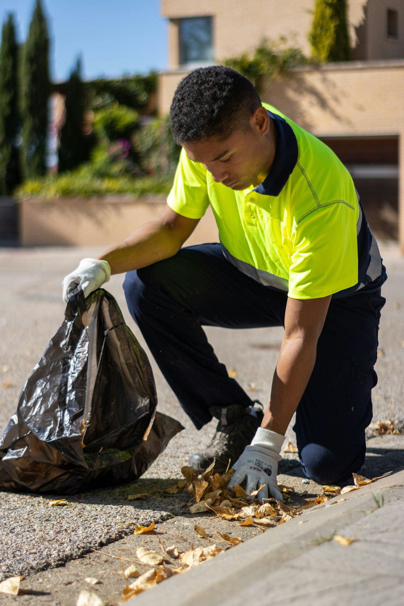 Vertical shot of a Latin man collecting autumn leaves and putting them into a trash bag